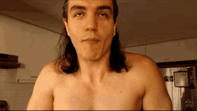 a shirtless man with long hair is looking up at the camera