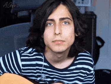 a young man with long hair is holding a guitar and wearing headphones .