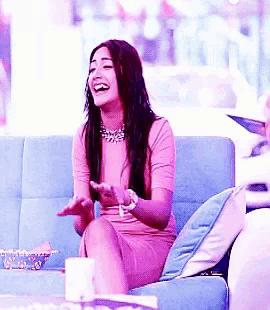 a woman in a pink dress is sitting on a couch laughing