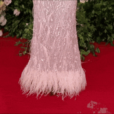 a woman in a white dress with white feathers on the bottom is standing on a red carpet