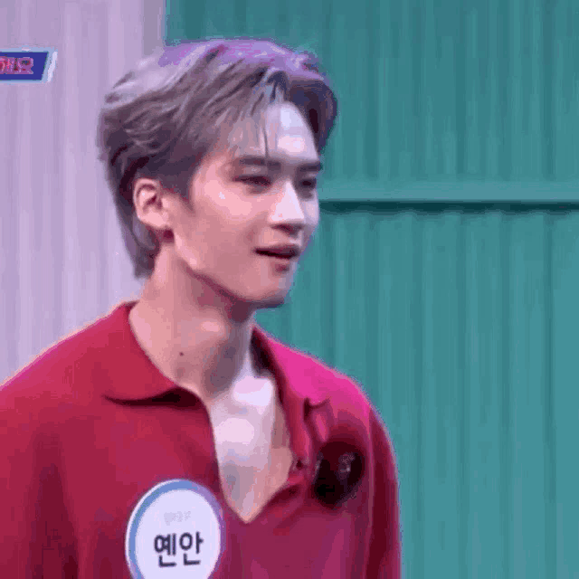 a young man in a red shirt is standing in front of a green wall and looking at the camera .