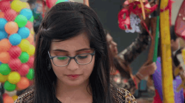 a girl wearing glasses is looking down in front of a bunch of colorful balls