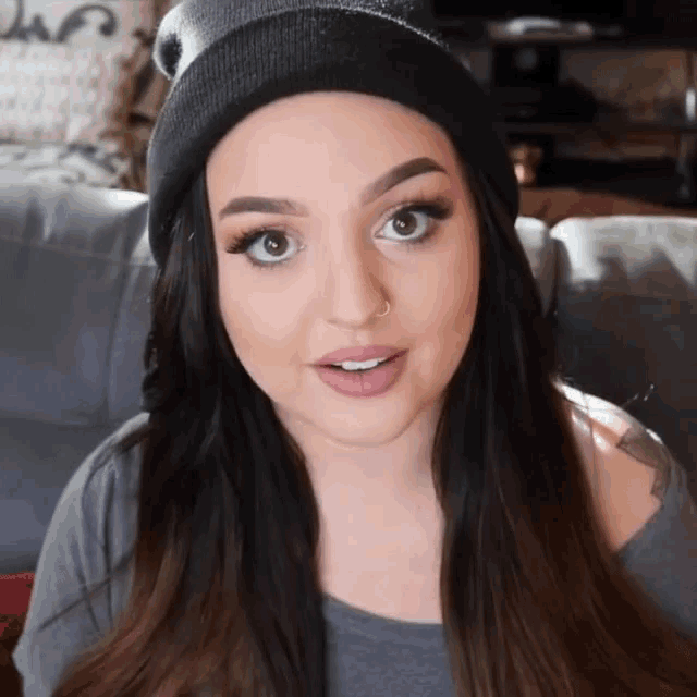 a woman wearing a beanie and a grey shirt looks at the camera