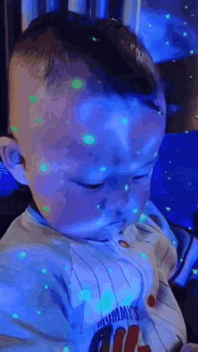 a baby is sitting in front of a blue light with green lights on his face .
