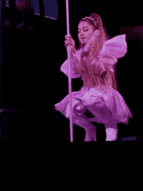 ariana grande is holding a pole on stage while wearing a purple dress and thigh high boots .