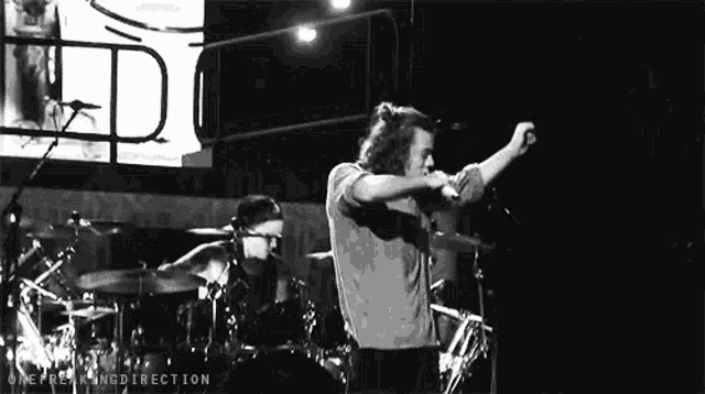 a black and white photo of a man singing into a microphone on stage .