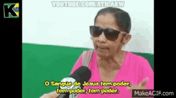 a woman wearing sunglasses and a pink shirt is talking into a microphone