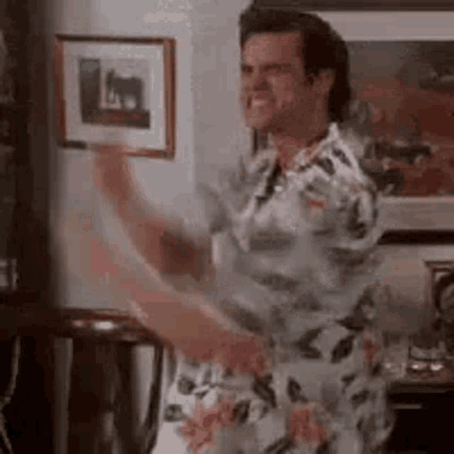 a man in a floral shirt is dancing in a living room in front of a picture .