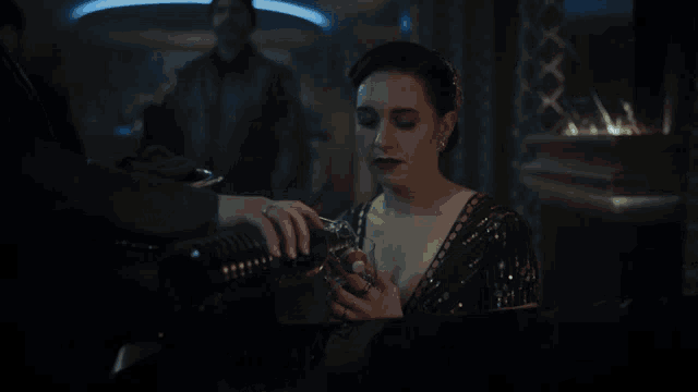 a woman in a black dress drinks from a glass in a dark room