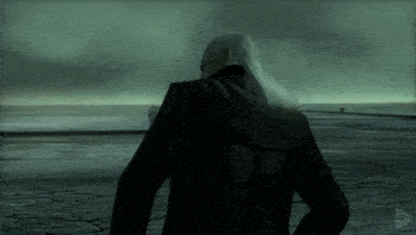 a man with long white hair in a black jacket stands in front of the ocean