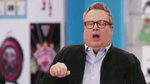 a man wearing glasses and a black jacket is pointing his finger at the camera .