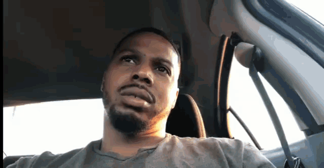 a man with a beard is sitting in the driver 's seat of a car looking at the camera .