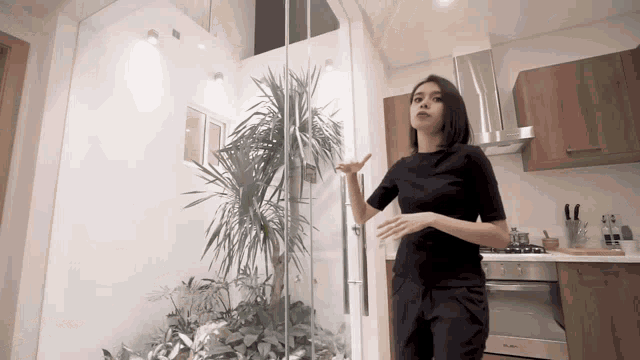 a woman in a black shirt is standing in a kitchen with a glass door
