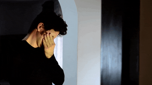a man in a black shirt covering his face with his hand