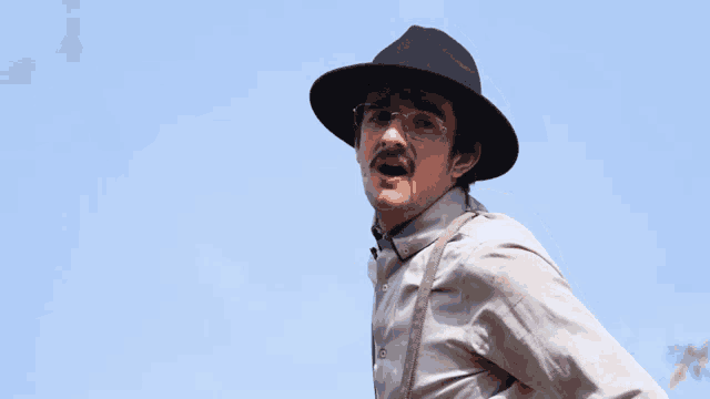 a man wearing a hat and suspenders makes a face