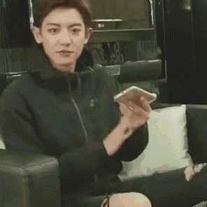 a young man is sitting in a chair holding a cell phone .
