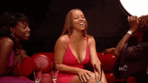 a woman in a red dress sits on a red couch next to two other women and a mc logo