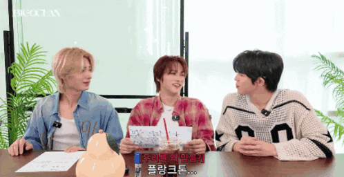 a group of young men are sitting at a table and one of them is wearing a big ocean shirt