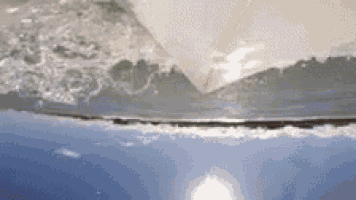 a close up of a wave breaking on a beach with a blue sky in the background