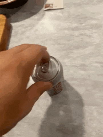 a close up of a person opening a can of soda on a table .