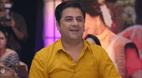 a man in a yellow shirt is smiling while sitting in front of a group of people .