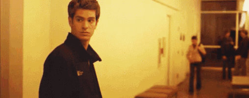 a young man in a black jacket is standing in a hallway looking at the camera .