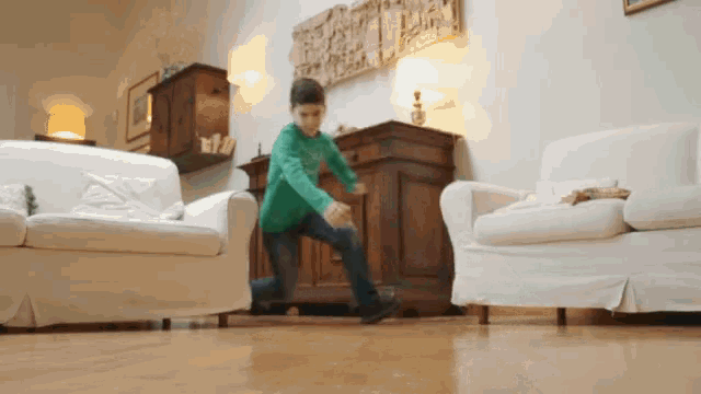 a young boy in a green shirt is running in a living room between two white couches