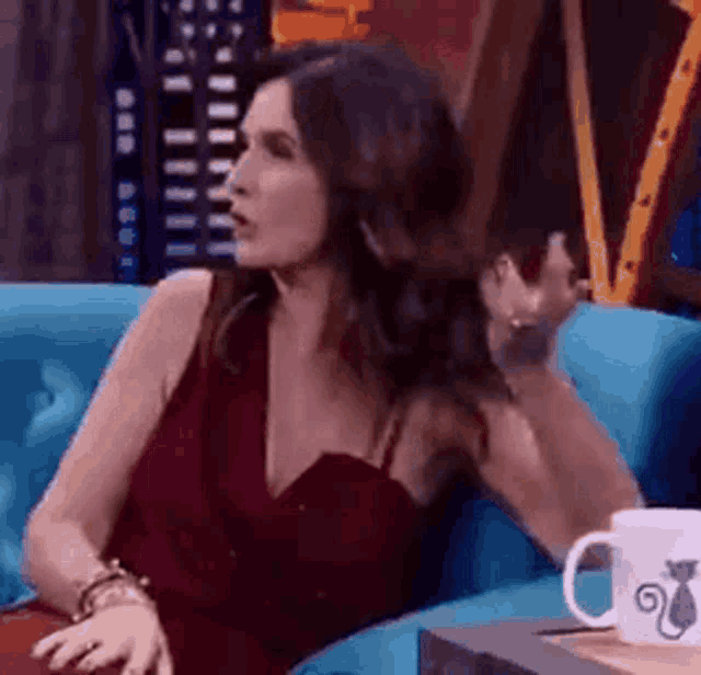 a woman in a red dress is sitting on a blue couch next to a coffee mug .