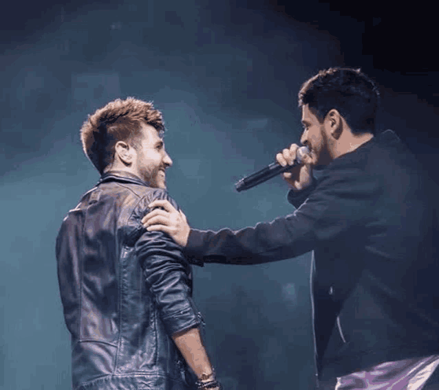 two men are standing next to each other and one is holding a microphone