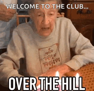 an elderly woman is sitting at a table with candles in her hands and says welcome to the club over the hill .