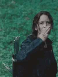 a woman is holding her hand to her mouth while standing in the grass .