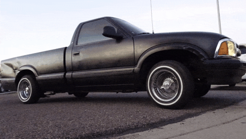 a black truck with white tires is parked on the side of a road