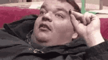 a fat man is laying on a couch holding something to his forehead .