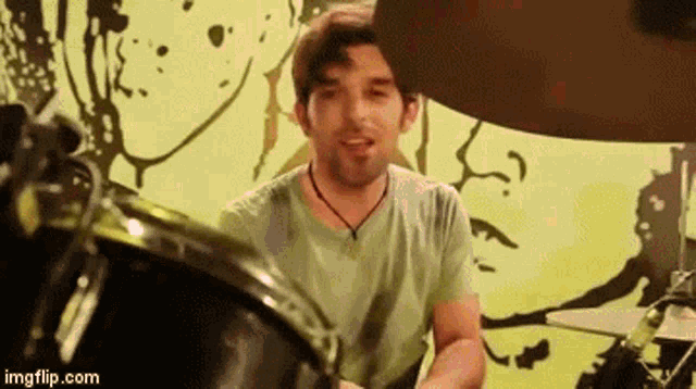 a man in a green shirt is playing drums in front of a yellow background .