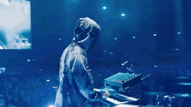 a man in a hooded jacket is playing a keyboard in front of a crowd