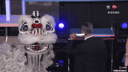 a man in a suit stands in front of a lion costume that says rhk31 on the screen