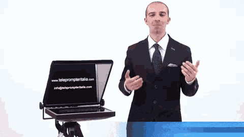 a man in a suit and tie is standing in front of a laptop that says teleprompteritalia.com