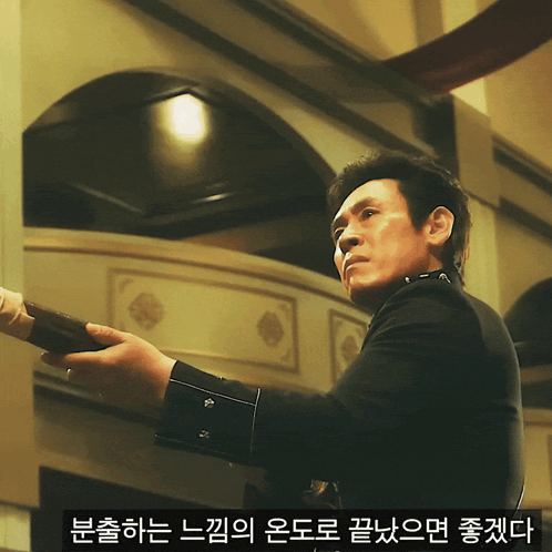 a man in a black uniform holds a sword in front of a wall with foreign writing on it