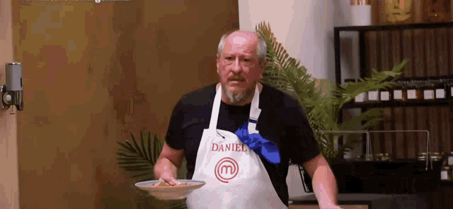 a man in an apron is holding a plate of food and making a funny face .