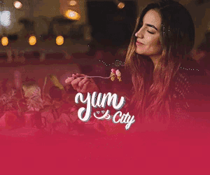 a woman is eating a piece of food with the words yum city written on the bottom