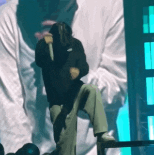 a man in a black hoodie is singing into a microphone on stage