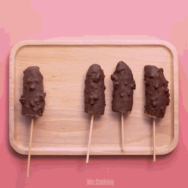 a wooden tray with four chocolate covered bananas on sticks