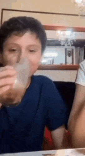 a young boy is sitting at a table drinking a glass of milk .