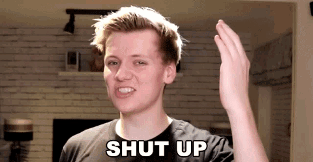 a man in a black shirt says shut up with his hand up