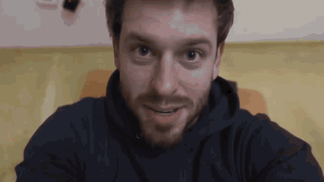 a man with a beard wearing a black hoodie smiles for the camera
