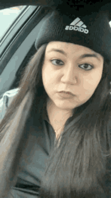 a woman wearing an adidas beanie is sitting in a car