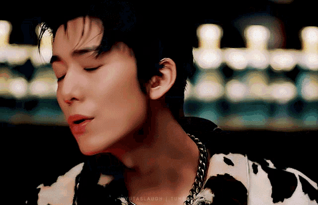 a close up of a man wearing a cow print shirt and a chain around his neck