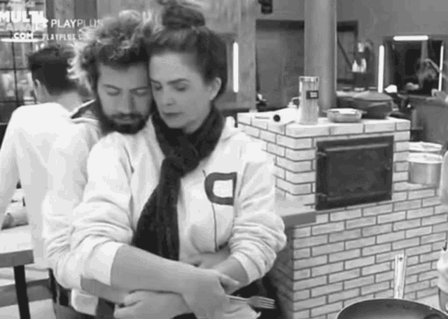 a black and white photo of a man and a woman hugging each other in a kitchen .