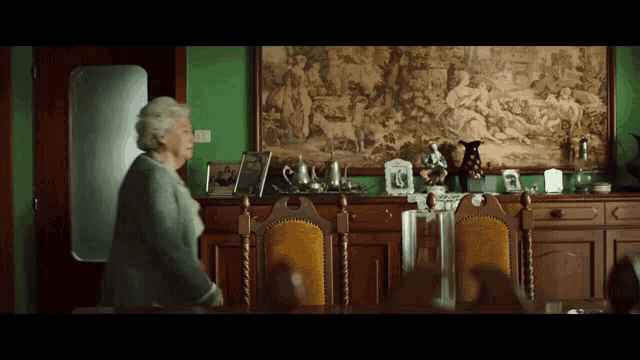 an elderly woman is standing in front of a dining room table and chairs
