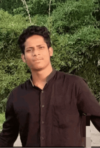 a young man wearing a black shirt is standing in front of trees .